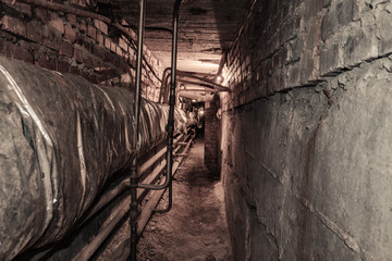 A long tunnel of an old abandoned basement. Basement with pipes and lamps on the sides