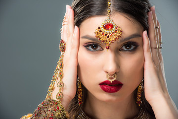 beautiful indian woman with bindi touching head, isolated on grey
