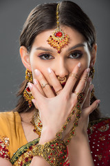 beautiful indian woman with bindi closing face with hands, isolated on grey