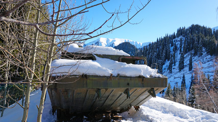 Abandoned military vehicles in the snowy mountains. Retro off-road machine military years. Machine in the mountains and forest. Blue sky and shadows. Abandoned tank on top of a hill. 