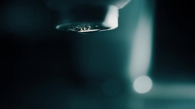 Slow motion shot of water drops falling from the faucet in dark bathroom