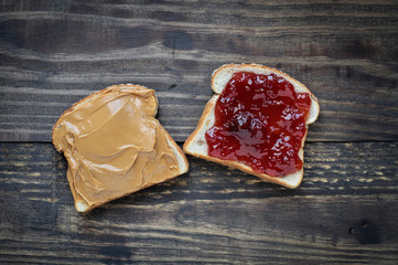 Top view of open face homemade peanut butter and strawberry Jelly sandwich on oat bread, over a rustic wooden background.