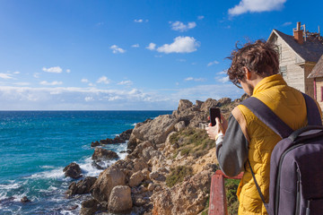 Man tourist taking photo on smartphone. Sea landskape in winter Malta