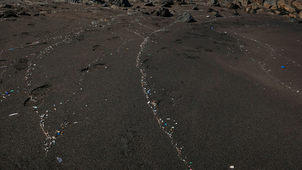 Plastic particles washed up by the waves on a beautiful black sand beach, damaging effect of human pollution, impacting the environment and affecting the marine ecosystem