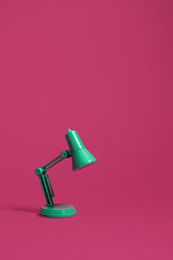 Bent over retro green desk lamp turned off and on a bright pink background.  Vertical composition with copy space and room for text.