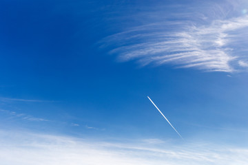 Airplane trail in the blue sky with clouds