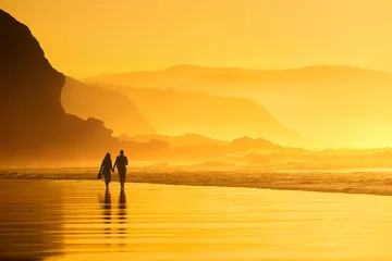 Fototapeten Paar, das bei Sonnenuntergang am Strand spazieren geht © mimadeo