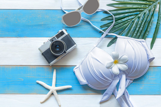 Summer  accessories, white bikini , camera and sunglasses go to travel in the beach. Tropical sea. Unusual top view. Travel and Summertime Concept.