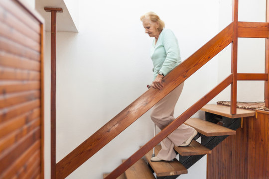Elderly woman at home using a cane to get down the stairs