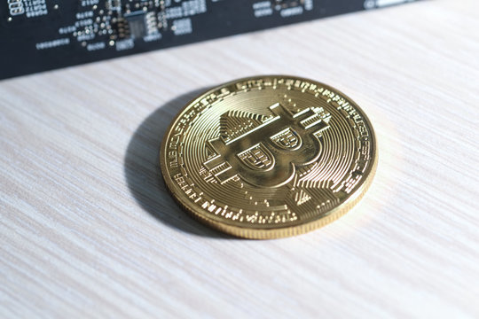 The symbol of gold bitcoin electronic coin on the table and an electronic circuit board on the side. Cryptocurrency golden bitcoin coin