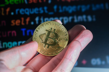 A hand holding a gold coin with a lot of lines of programming code as a background. Cryptocurrency...