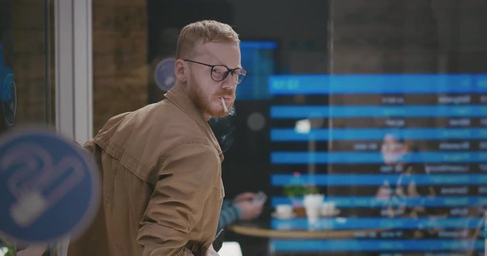 Young stylish guy at the bus station comes into the smoking room