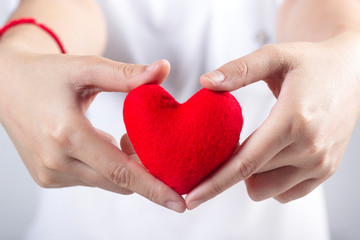 Woman's hands with white t-shirt holding red fabric heart shaped