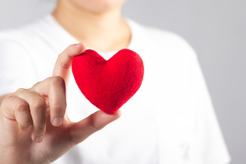 Woman's hand with white t-shirt holding red fabric heart shaped