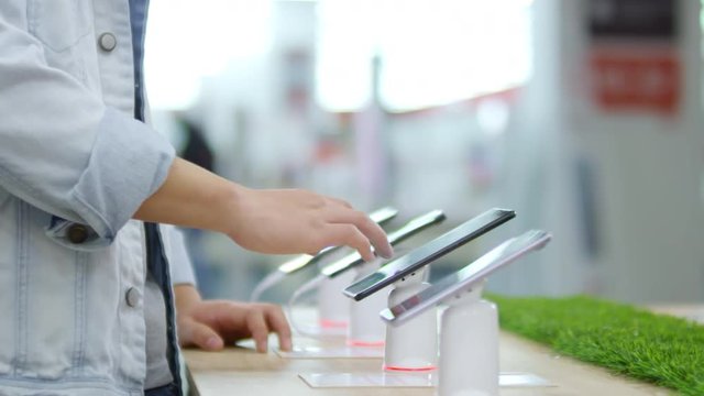 Close up hand of unrecognizable young man using touchscreen of smartphone when choosing between different models in gadget store