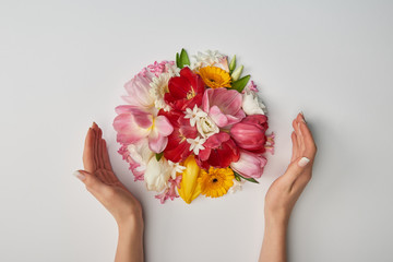 cropped view of female hands and  bouquet of flowers on white background