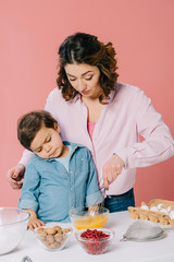 cute little boy attentively watching his mother whipping eggs isolated on pink