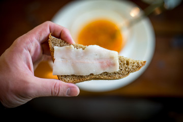 sandwich with salted lard in hand on the background of borscht.