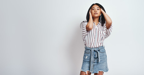 Studio shot of beautiful asian woman in casual wear playing with her hair and looking at camera standing in studio on a grey background