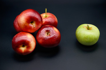 Five red apples and one green on black background