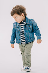 serious little boy in blue jacket and green jeans isolated on white