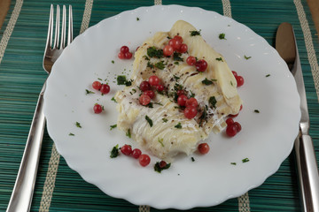 Boiled cod fillet with berries, herbs and spices on a plate close-up. Dietary healthy food.