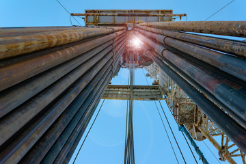 Fototapeta premium Oil and Gas Drilling Rig onshore dessert with dramatic cloudscape. Oil drilling rig operation on the oil platform in oil and gas industry. Land drilling rig blue sky