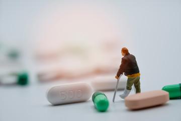 Miniature of old man broken legs model around with Pharmaceutical medicine pills, capsules and tablets on white background. Copy space for add text - Image