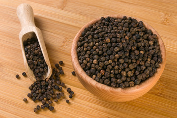 Black pepper peppercorns in wooden scoop and jar on bamboo desk. Top view.