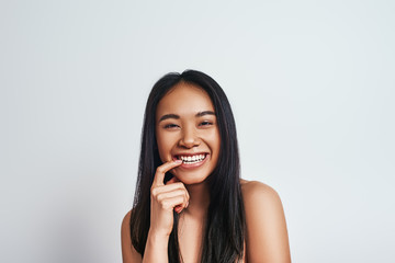 Having fun. Close up portrait of young beautiful asian woman looking at camera and smiling while standing on a grey background. Positive emotions