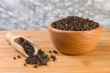 Black pepper peppercorns in wooden scoop and jar on bamboo desk. Closeup.