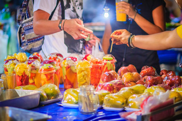 Close up street fruit vendor selling mixed fruits at Khao San Road night market, Bangkok, Thailand.