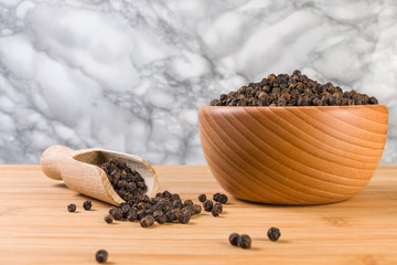 Black pepper peppercorns in wooden scoop and jar on bamboo desk. Closeup.