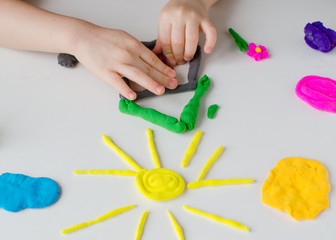 Child hands playing with colorful clay. Homemade plastiline. Kid make a house from plastiline. Colorful plastilin