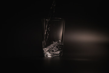 Water is poured into a transparent glass on a dark background