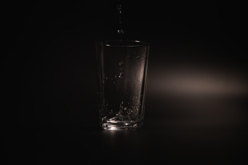 Water is poured into a transparent glass on a dark background