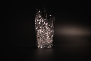 Water is poured into a transparent glass on a dark background
