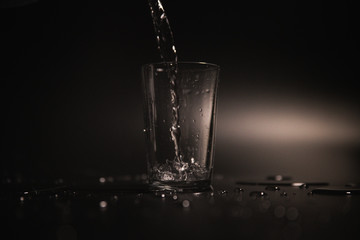 Water is poured into a transparent glass on a dark background