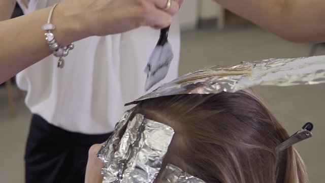 Hairdresser makes hair coloring. Close up of Hair stylist applying hair coloring dye to lighten up hair tone in slow motion.