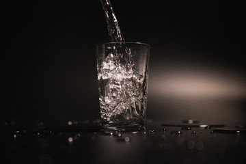Water is poured into a transparent glass on a dark background