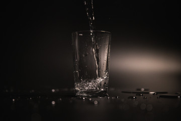 Water is poured into a transparent glass on a dark background