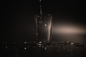 Water is poured into a transparent glass on a dark background