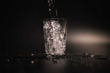 Water is poured into a transparent glass on a dark background
