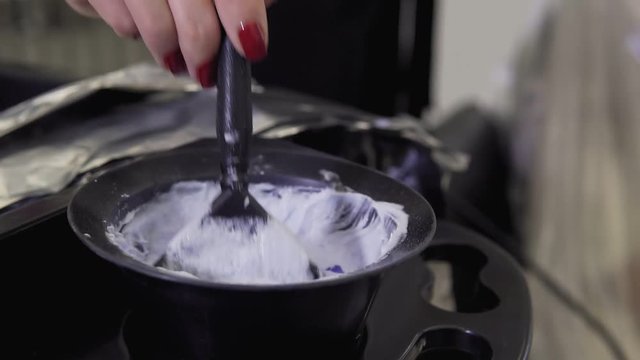 Hairdresser makes hair coloring. Close up of Hair stylist applying hair coloring dye to lighten up hair tone in slow motion.