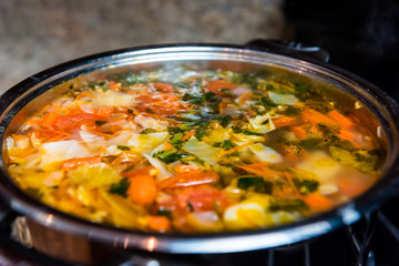 Large big pot of homemade vegetable soup macro closeup in kitchen in stainless steel container on stove cooking and nobody