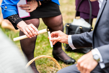 Ukrainian Orthodox Easter blessing wicker straw baskets with senior man and woman hand placing candle on grass ground outside at church with flame