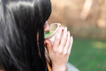 Woman girl black asian hair holding tea cup closeup drinking outside in backyard garden with green...