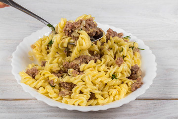 Spirals pasta Bolognese. Tagliatelle with minced meat on a white plate on a wooden background.