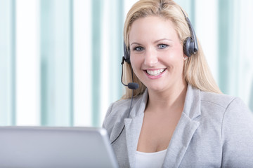Hübsche Hotline Mitarbeiterin mit Headset im Call Center lächelt