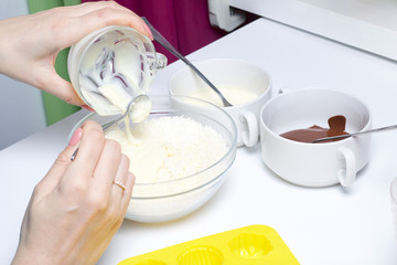 Woman adds condensed milk to coconut chips. Ingredients for dessert are on the table. Cooking sweets with coconut and condensed milk. In a glaze of white and black chocolate.